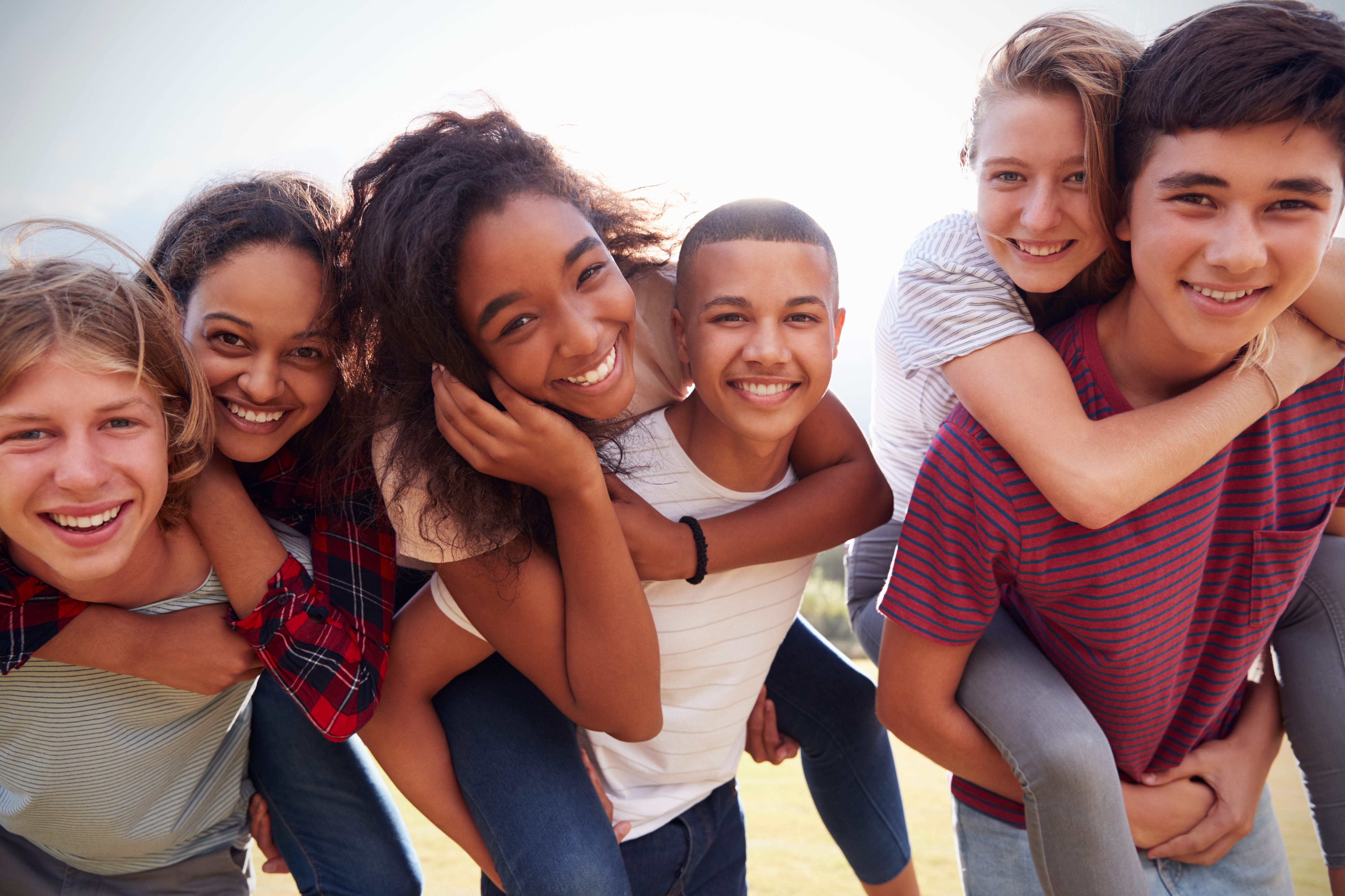 Outdoor shot of a group of teenagers smiling with some piggy backing on the backs of others.