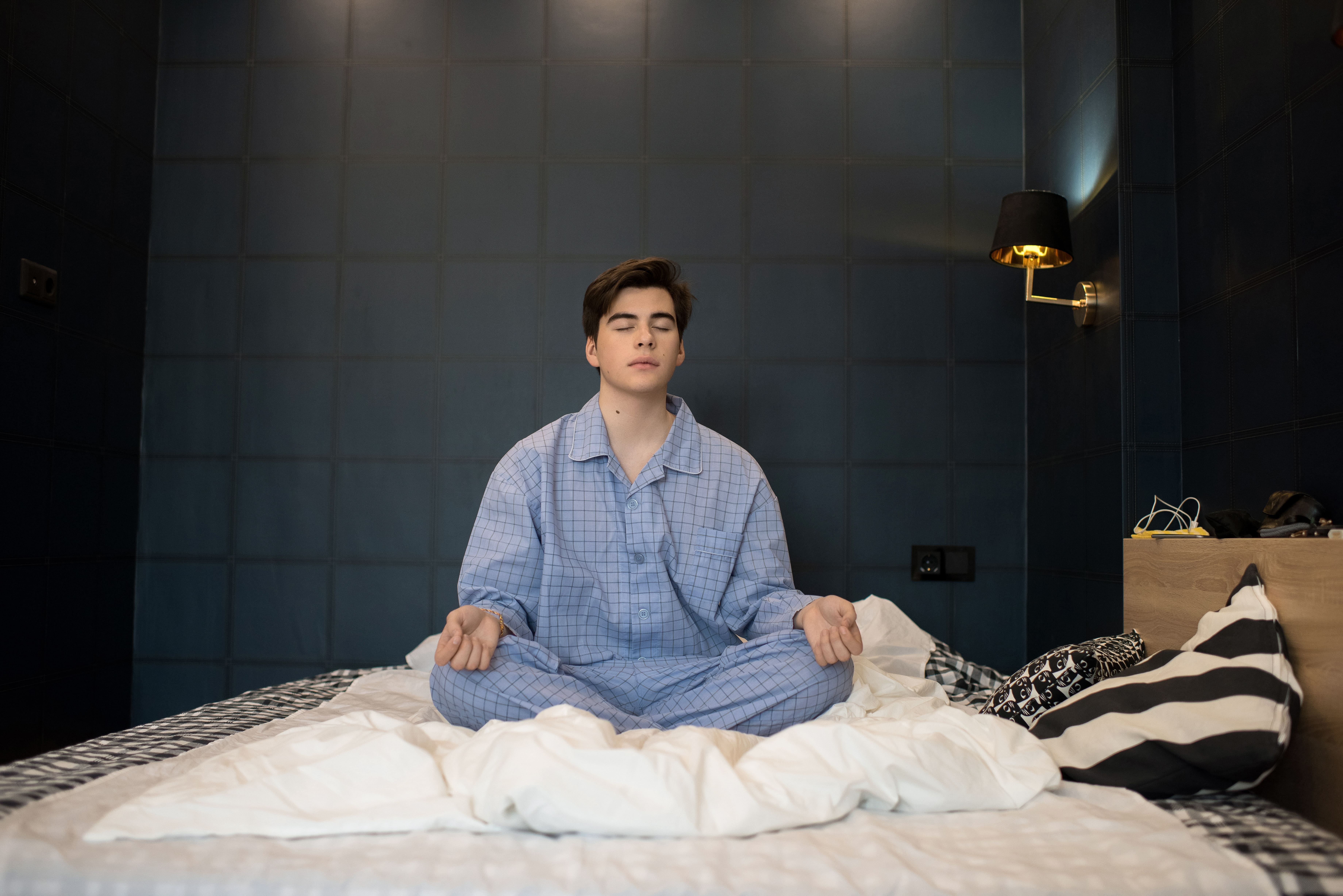 A man sat crossed legged on his bed as he practices meditation before turning out the light.