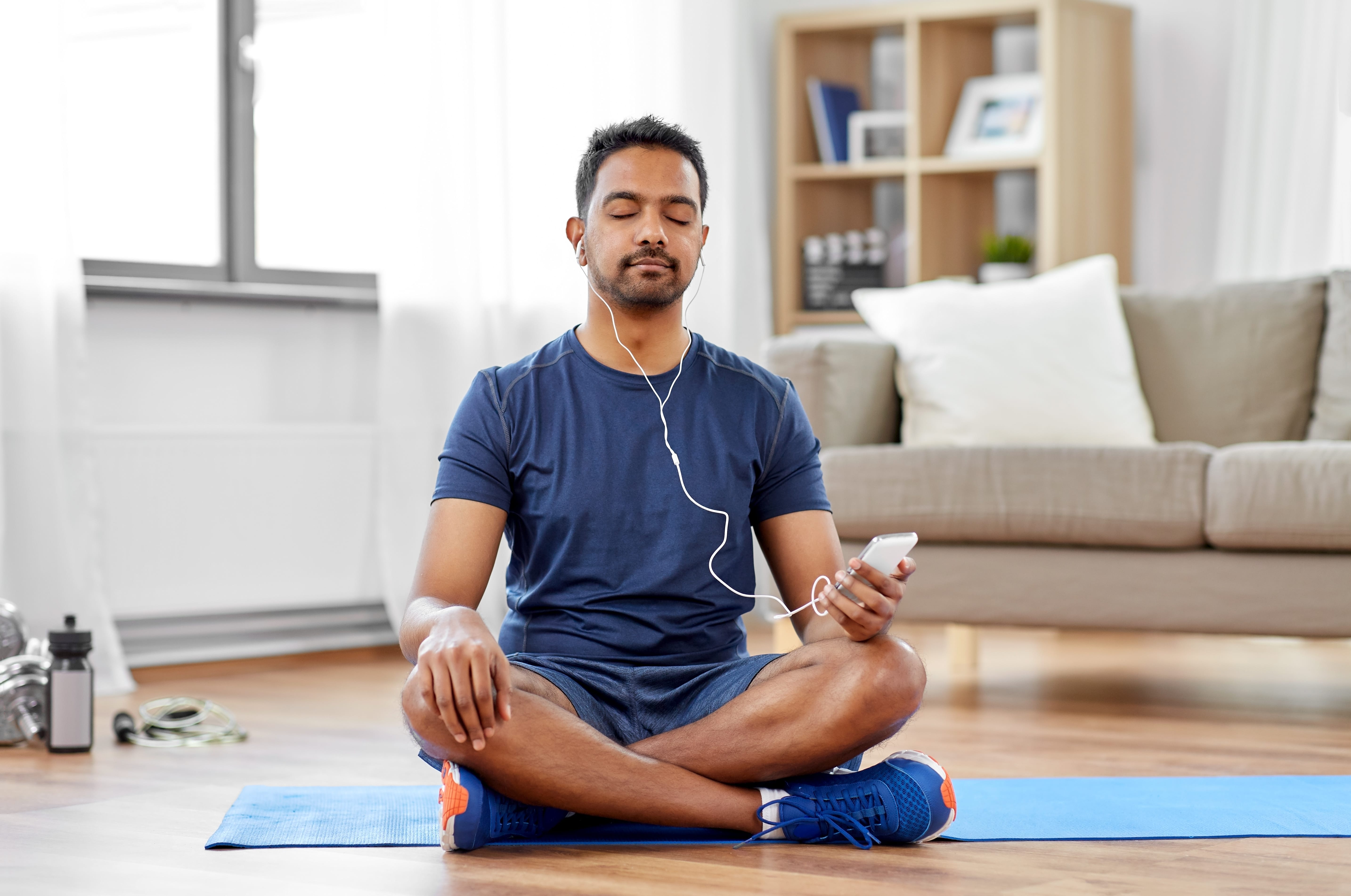 A man sat crossed legged on his living room floor practicing guided mindfulness meditation.