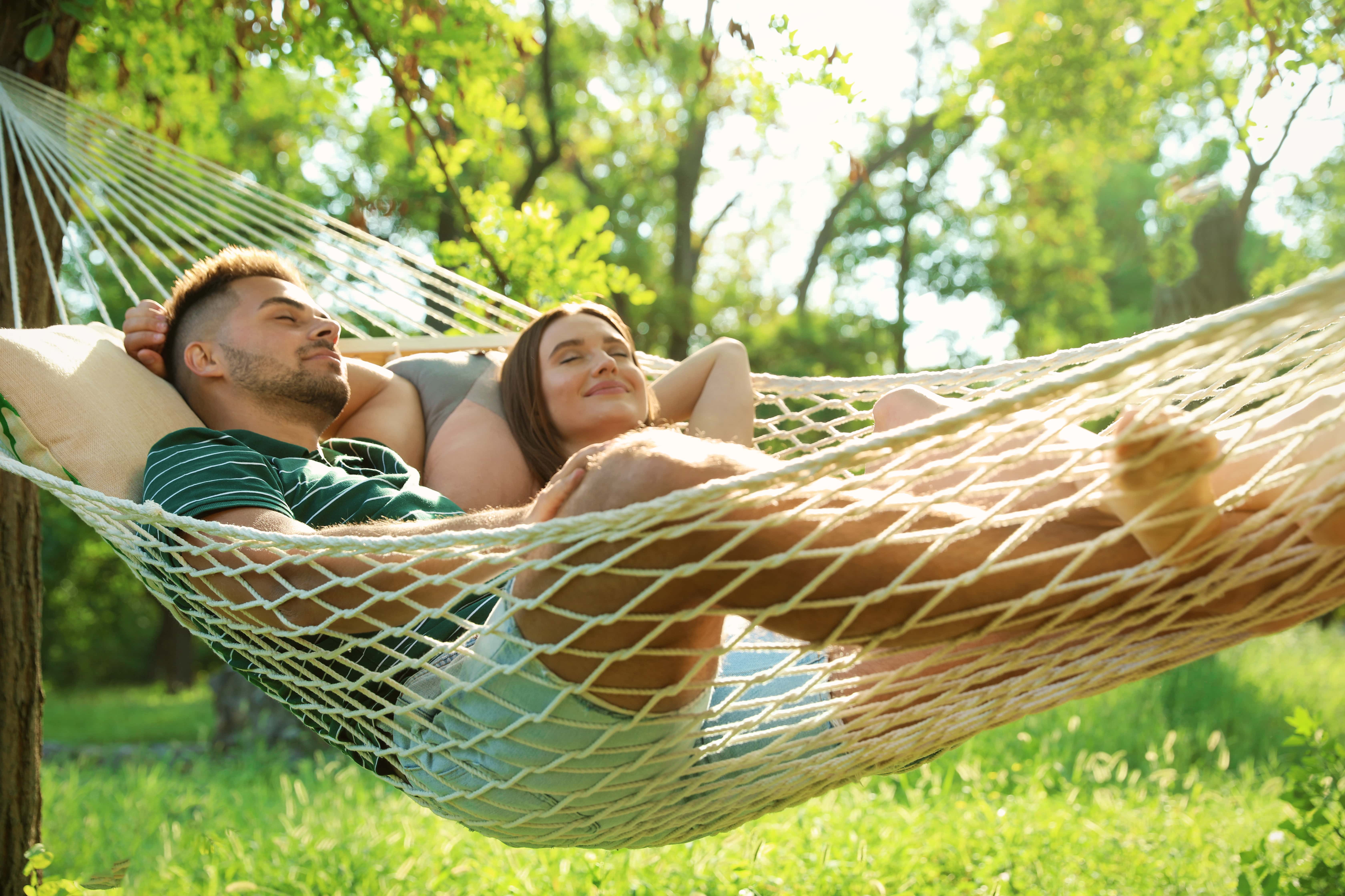 A couple snoozing in the sunshine sharing a hammock in their wooded and wild garden