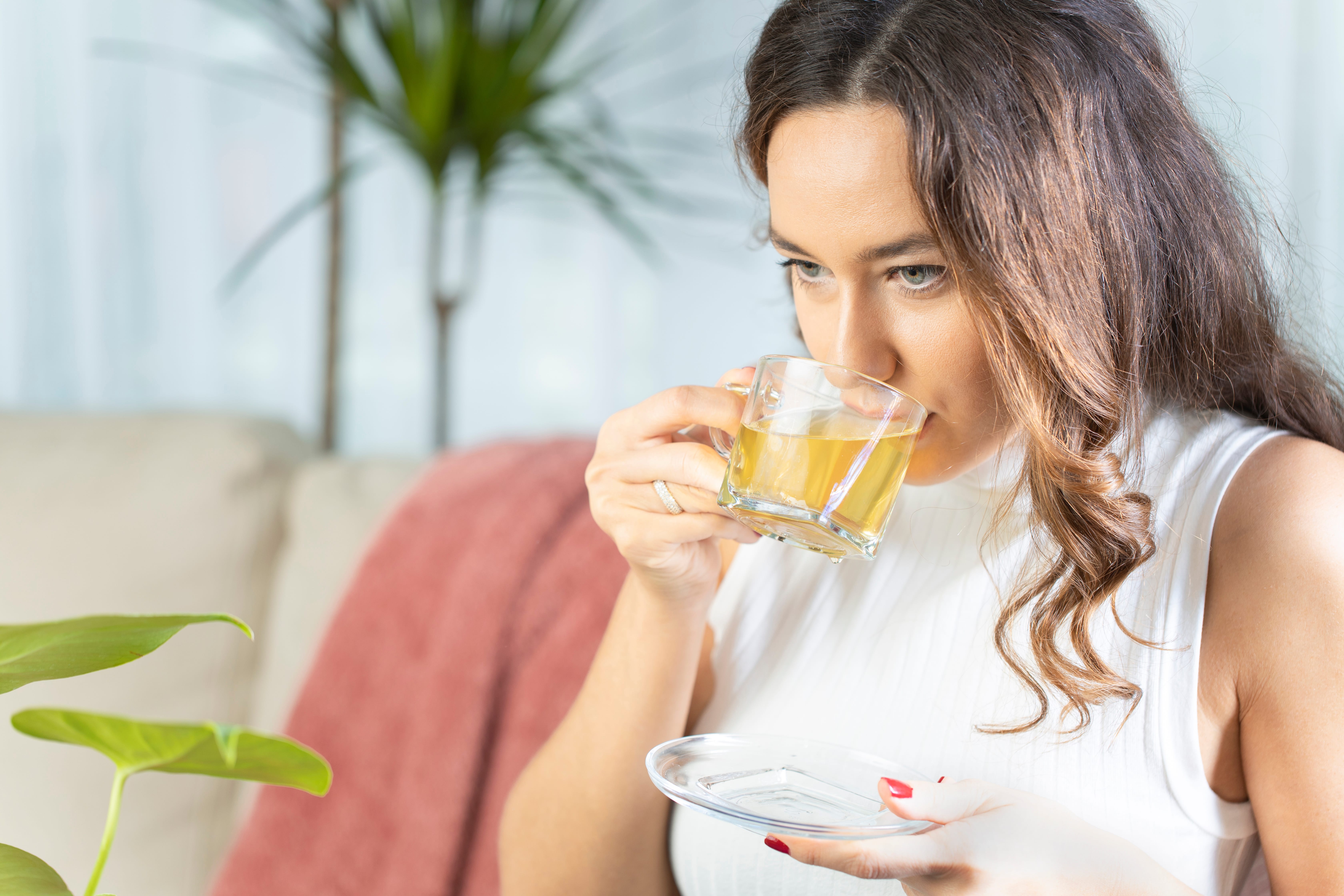 A lady sipping from a glass mug filled with herbal tea mindfully.