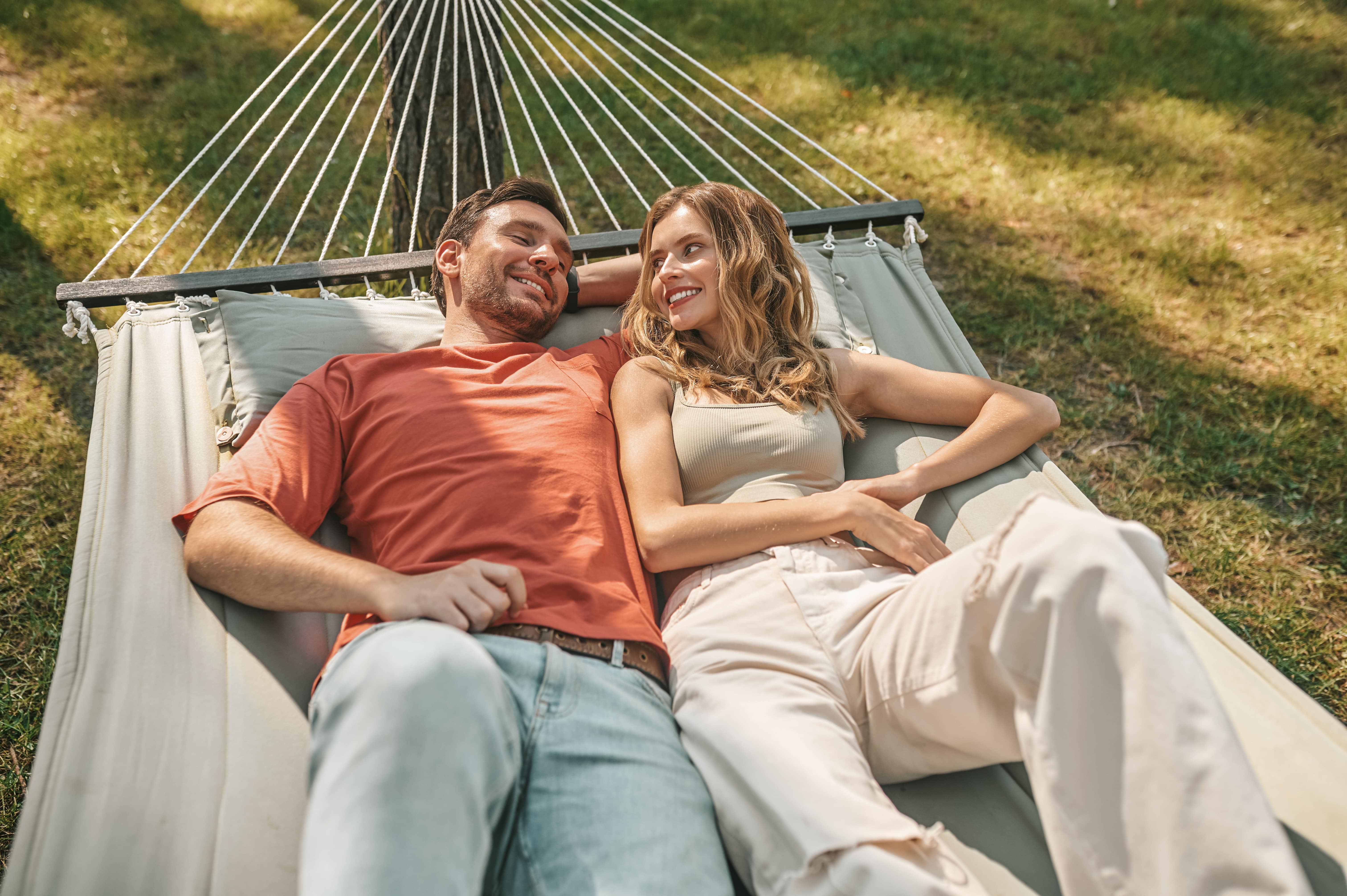 A man and woman cuddled together outdoors on a hammock relaxing in the sunshine