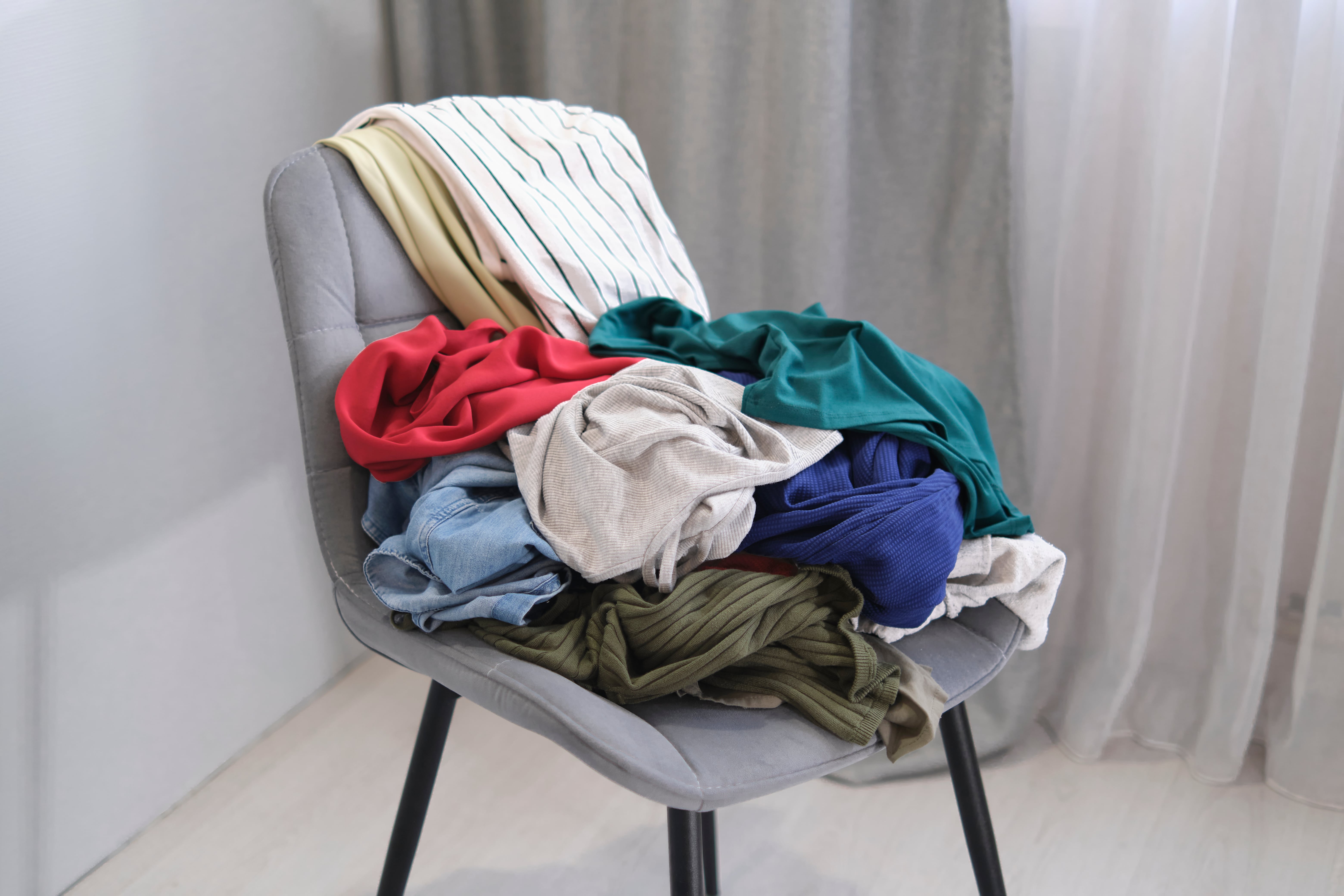 A chair in the corner of a bedroom covered in various items of clothing worn in the week.