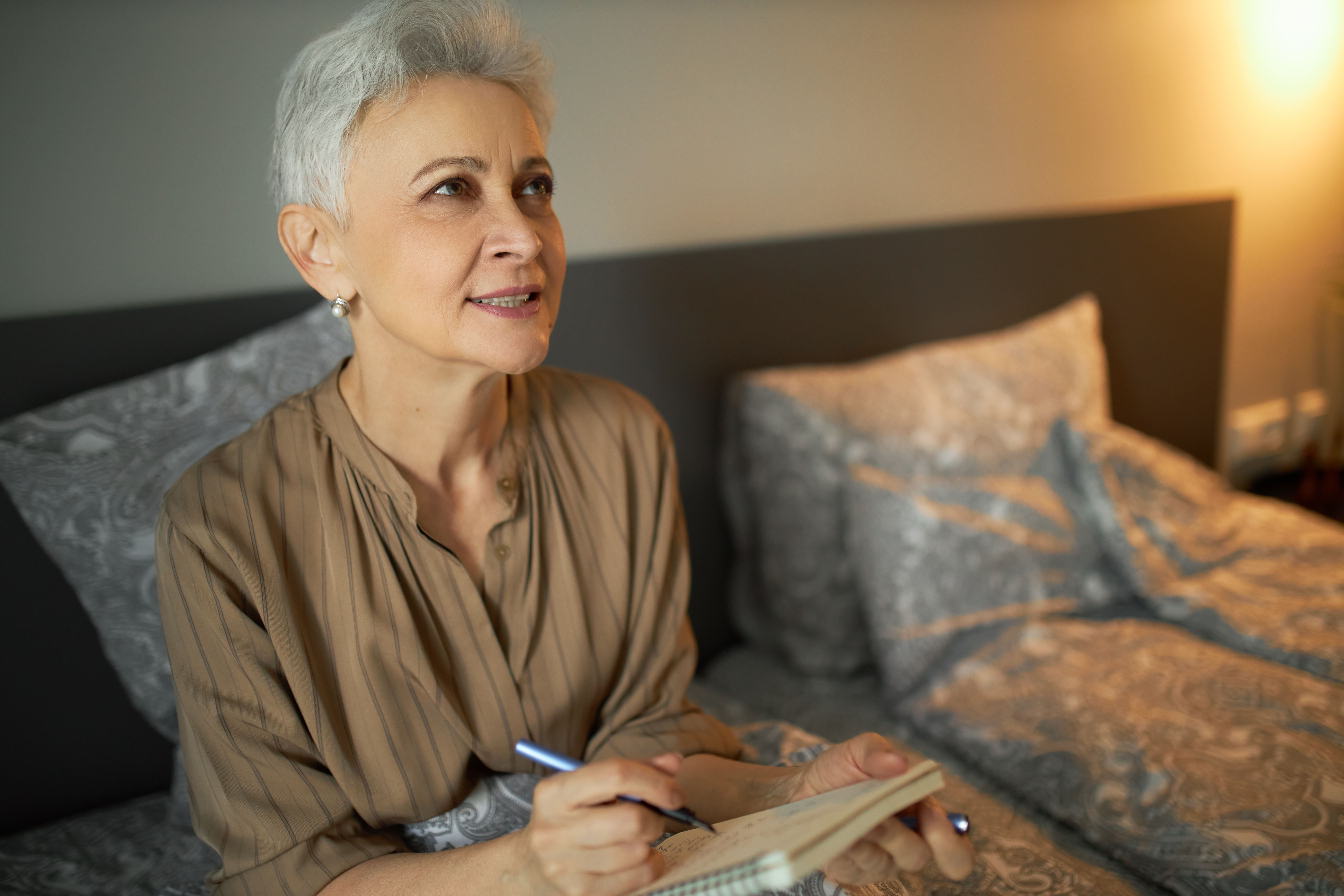 A lady sat in bed calculating last night's sleep efficiency with her sleep diary in her hand