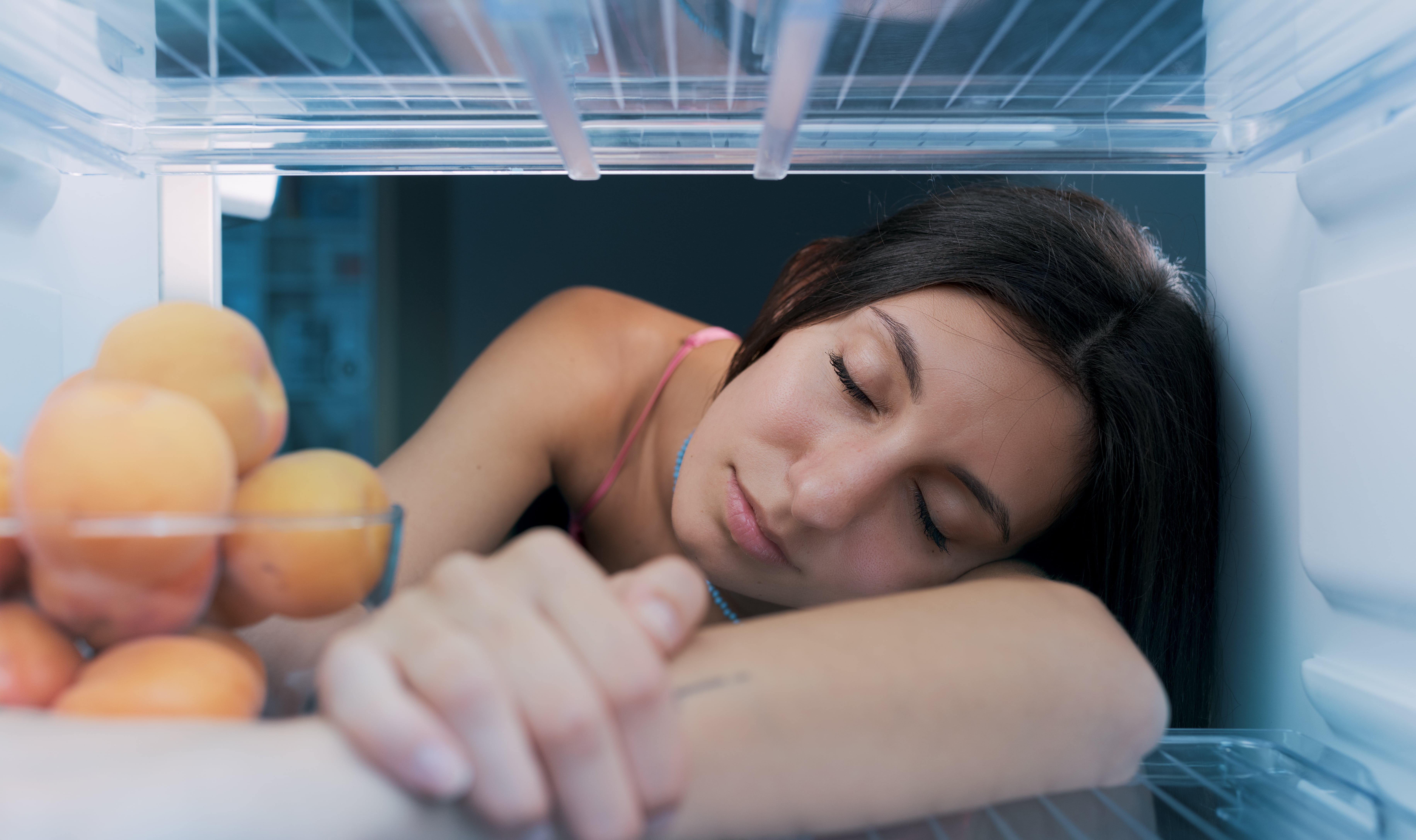 A woman asleep with her head in a fridge as she tries to get some sleep on a hot night