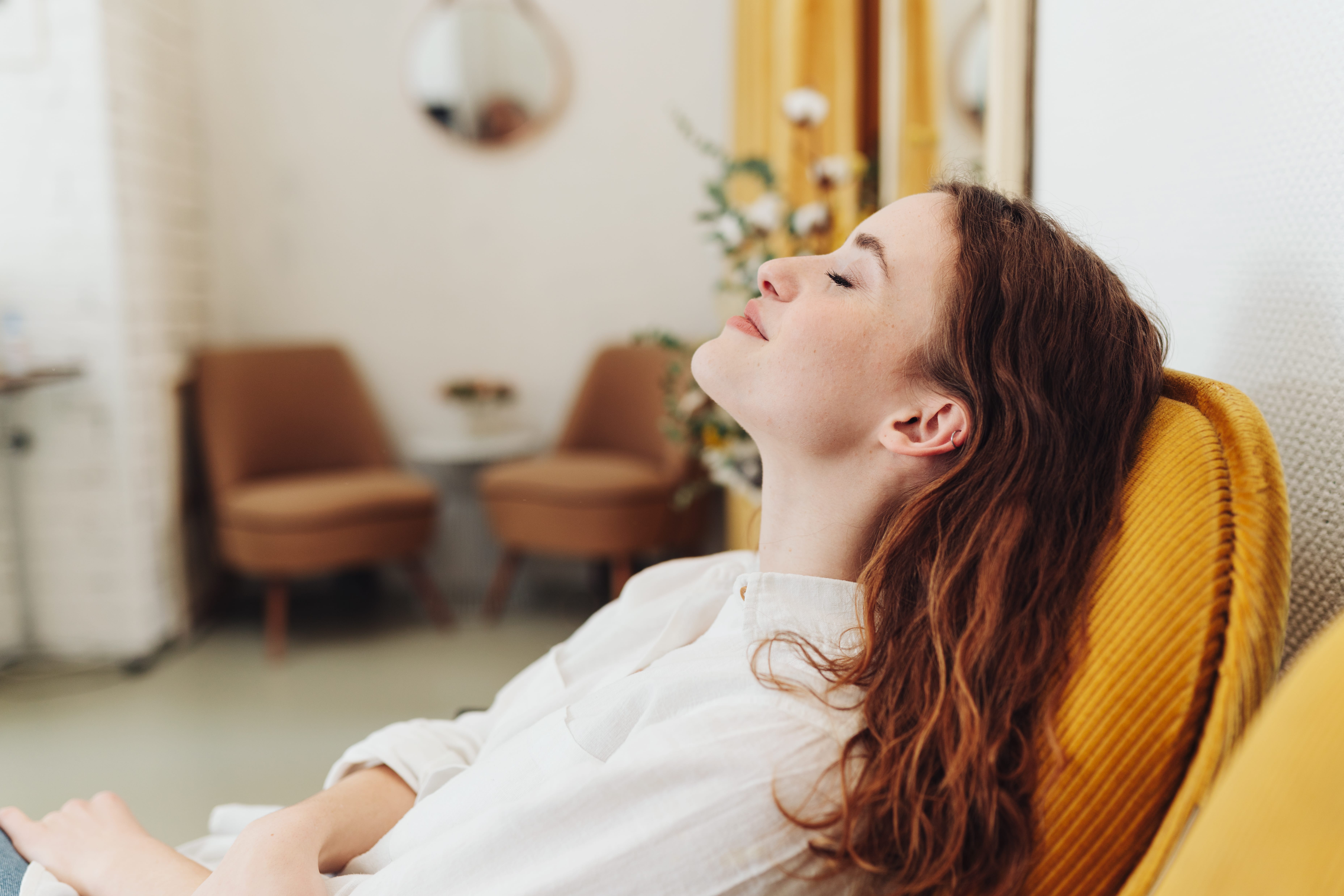 A lady reclining her head backwards and closing her eyes as she practices mindful meditation.