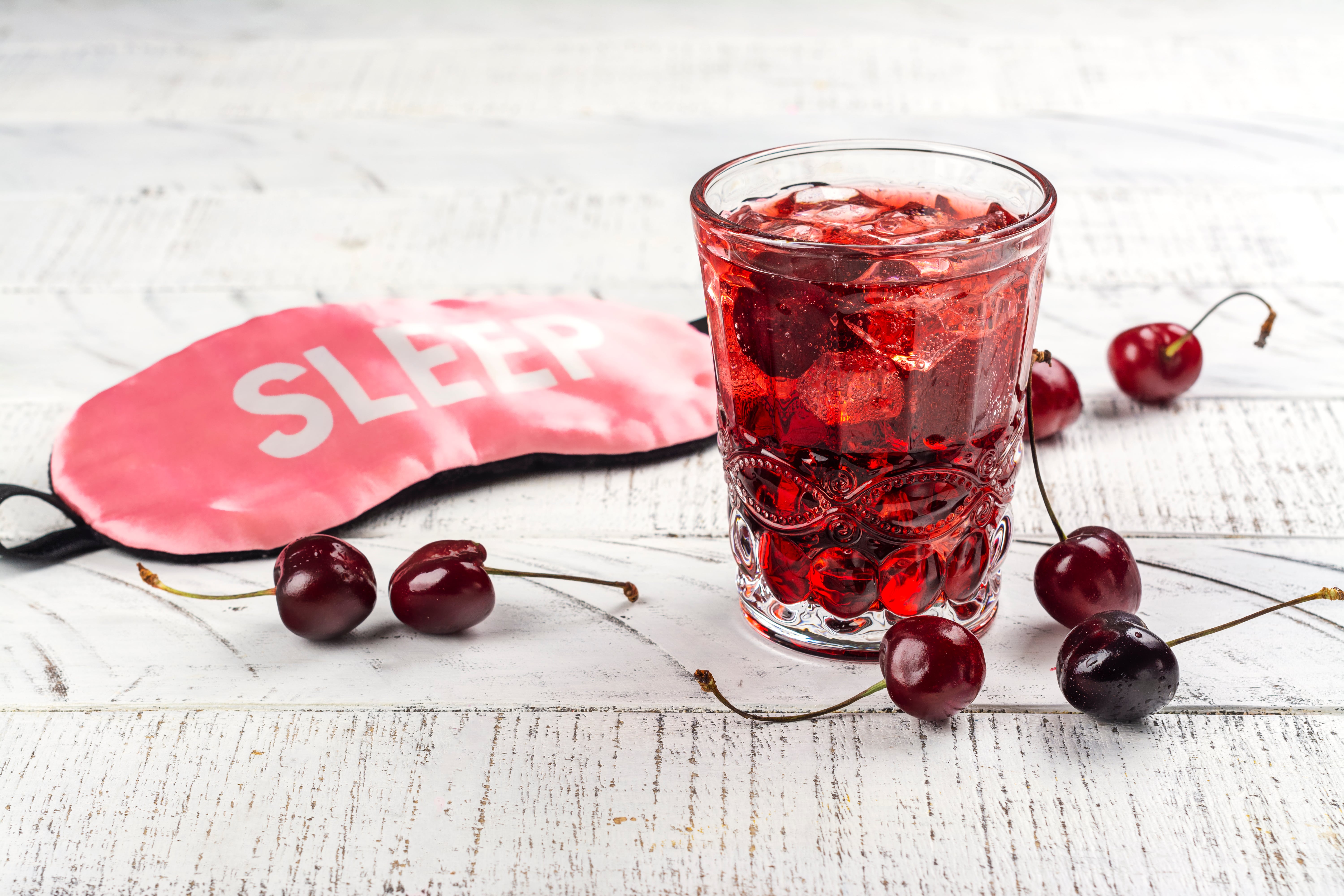 A cranberry sleep mocktail sat beside a sleep mask on a white washed wooden surface.