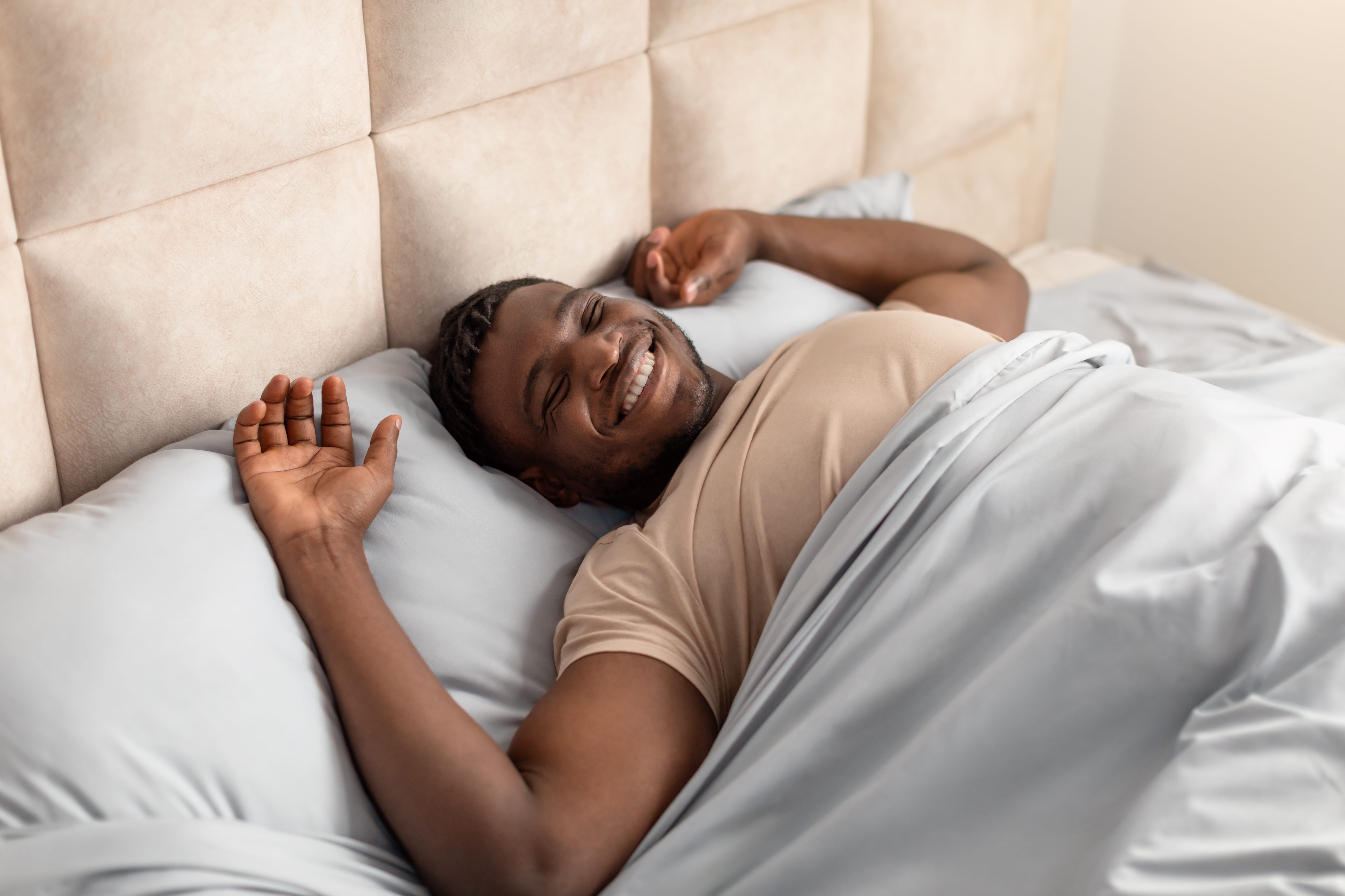 A man stretching and smiling in bed as he wakes up feeling refreshed and full of energy